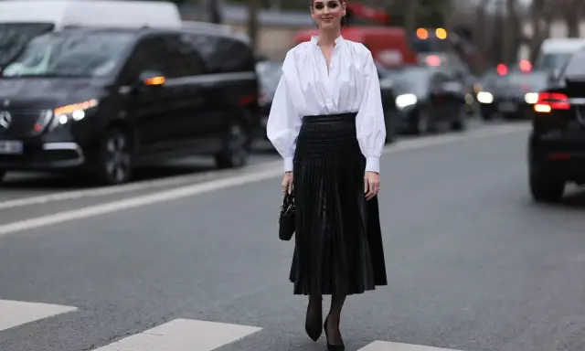Chic Frau in weißer Bluse und schwarzem oberteil zu plisseerock, steht auf Zebrastreifen.