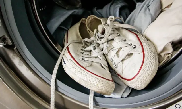 Weiße Turnschuhe mit roten Streifen liegen in einer Waschmaschine, bereit für die Reinigung.