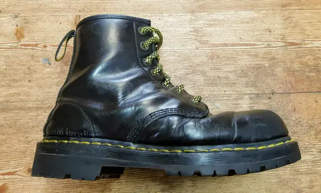 Schwarzer Dr. Martens Stiefel mit gelben Schnürsenkeln und einer neuen, robusten Sohle auf Holzuntergrund.