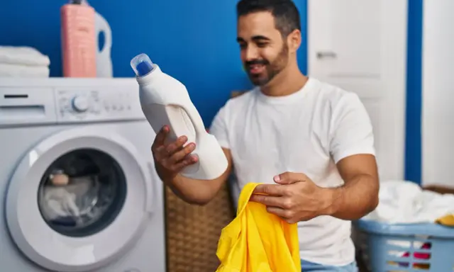 Mann hält Waschmittel und ein gelbes Trikot bereit, um die Wäsche zu waschen.