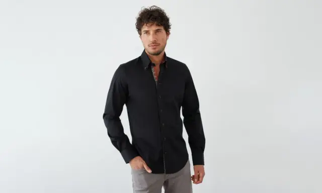 Mann in schwarzem Hemd mit farbigem Kragen und grauer Hose. Ein stilvoller Look, wie man ein schwarzes Hemd kombinieren kann.