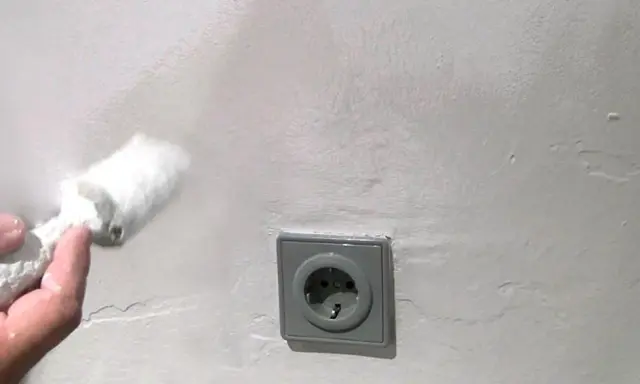 Mit einem Schwamm wird die Wand bearbeitet, um Wasserflecken zu entfernen. Eine Steckdose ist sichtbar.