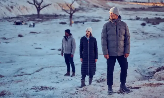 Drei Personen in Winterjacken stehen in einer verschneiten, kargen Landschaft. Die Frage "ab wann Winterjacke" stellt sich bei diesem Anblick von selbst.
