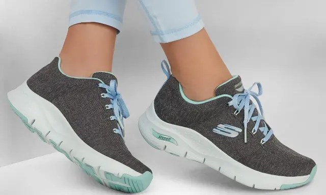 Graue Skechers-Sneaker mit hellblauen Schnürsenkeln und mintgrünen Akzenten. Die Sohlen zeigen die Skechers Sohlen Unterschiede, mit einer markanten ArchFit-Technologie.