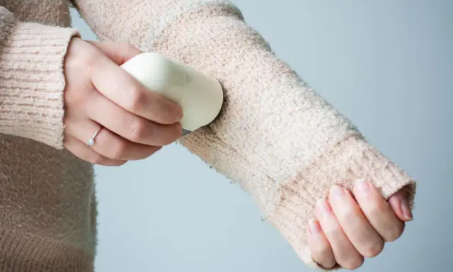 Frauenhand entfernt mit einem Hausmittel Fussel von einem Strickpullover.
