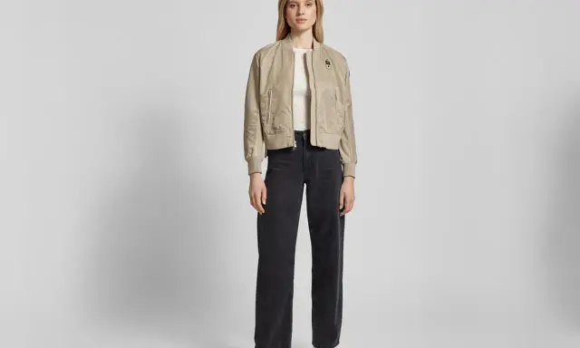 Frau stylt eine beige Bomberjacke mit weiten schwarzen Jeans und weißen Sneakern. Ein lässiger Look, der sich leicht anpassen lässt.