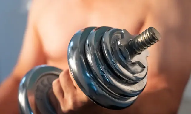Mann hebt Hantel. Die Frage "wie lange dauert muskelaufbau" beschäftigt viele Fitnessbegeisterte.