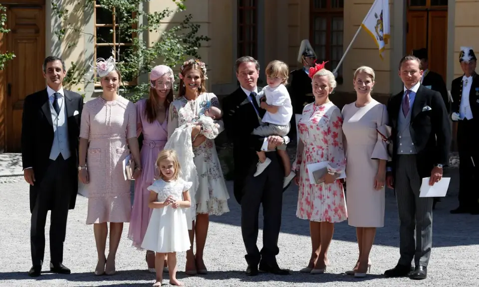 Familie in festlicher Kleidung, die überlegt, was anziehen zur Taufe. Ein Mann trägt ein Baby, Kinder und Frauen in eleganten Kleidern.