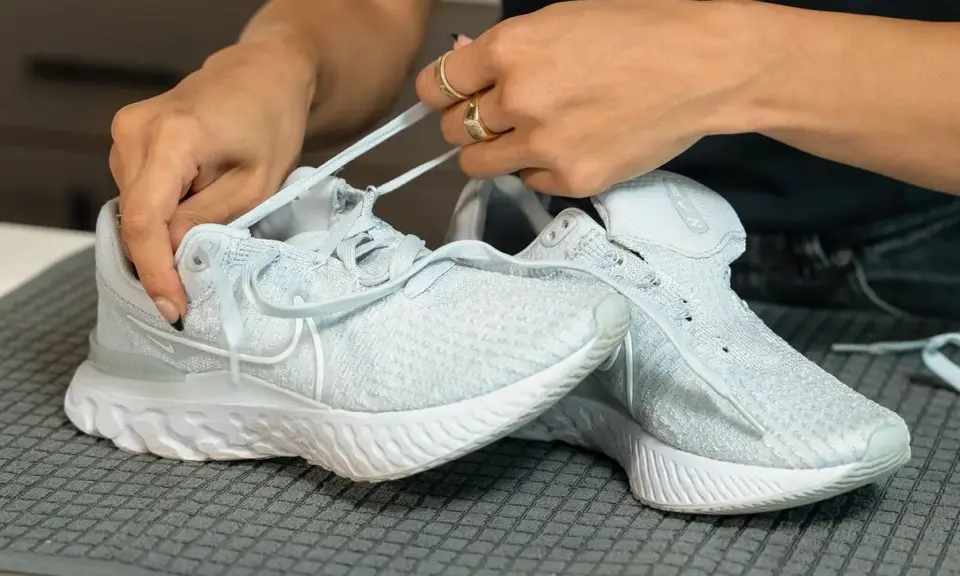 Hände ziehen Schnürsenkel durch hellblaue Mesh Schuhe. So einfach lassen sich die Lieblingssneaker reinigen.