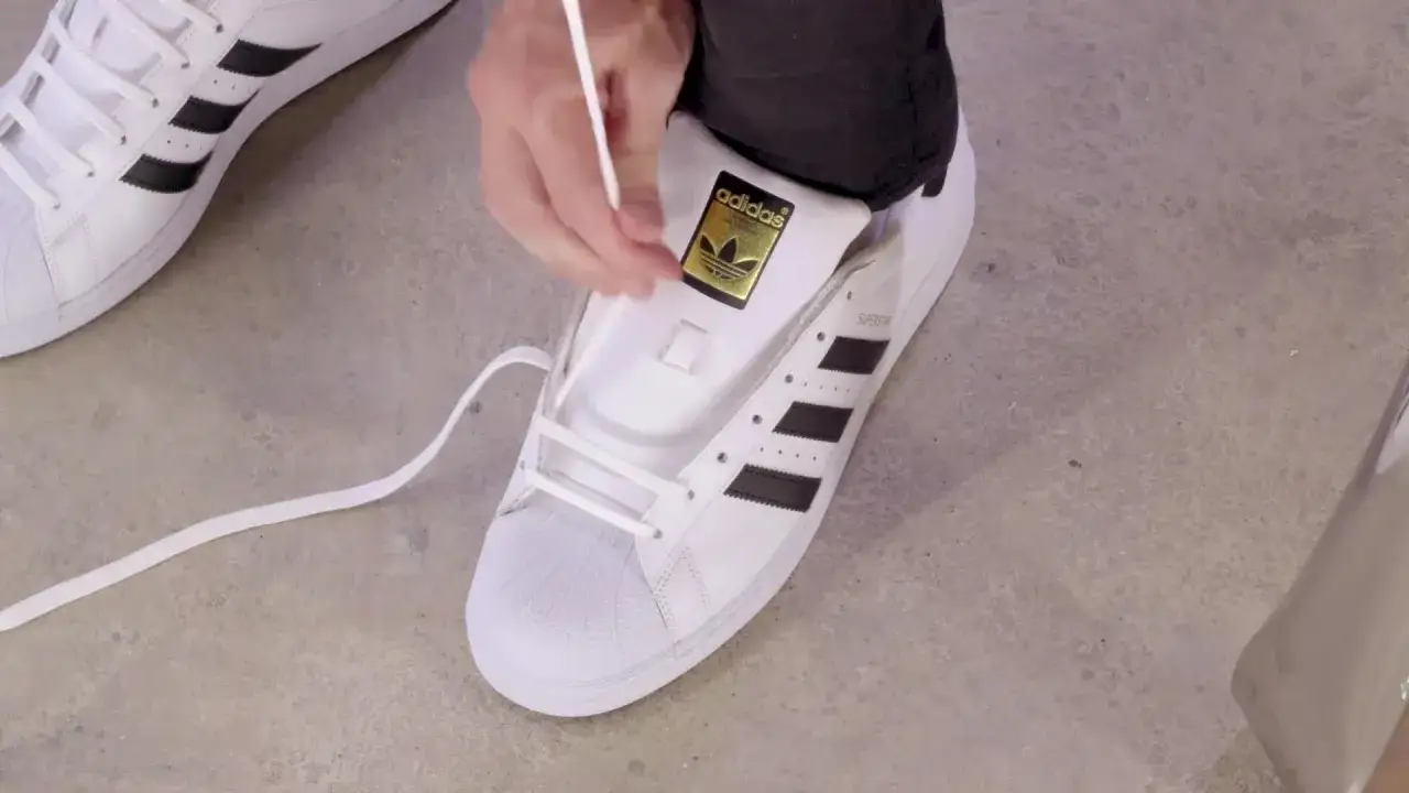 Person bindet weiße adidas schuhe. Die Schnürsenkel werden durch die Ösen gezogen.