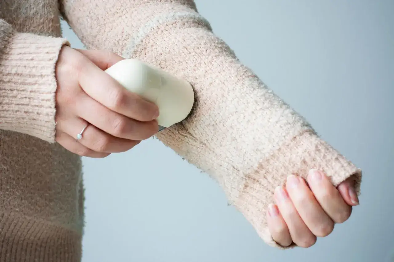 Eine Hand entfernt mit einem praktischen Hausmittel Fusseln von einem Pullover.
