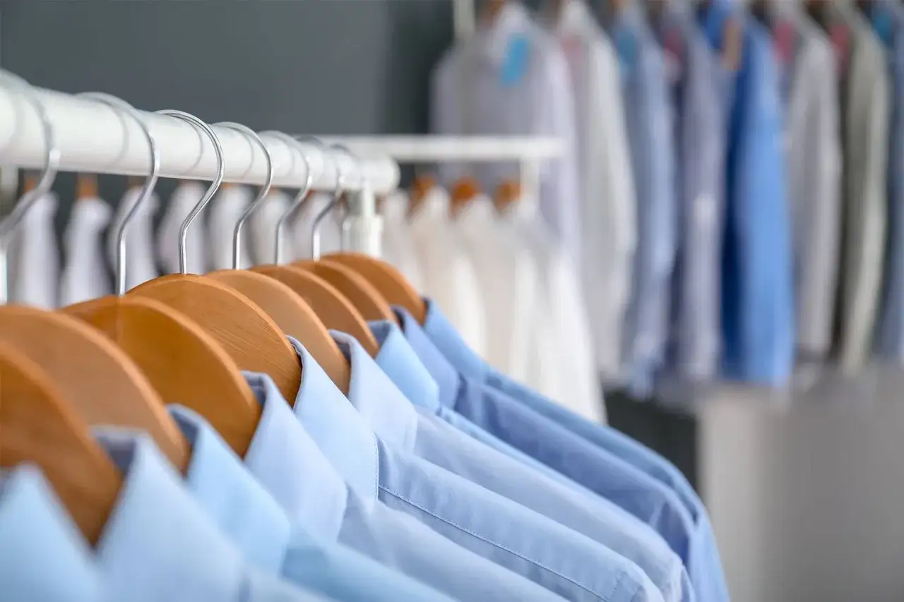 Reihe von blauen und weißen Hemden auf Kleiderbügeln, bereit für die chemische Reinigung.
