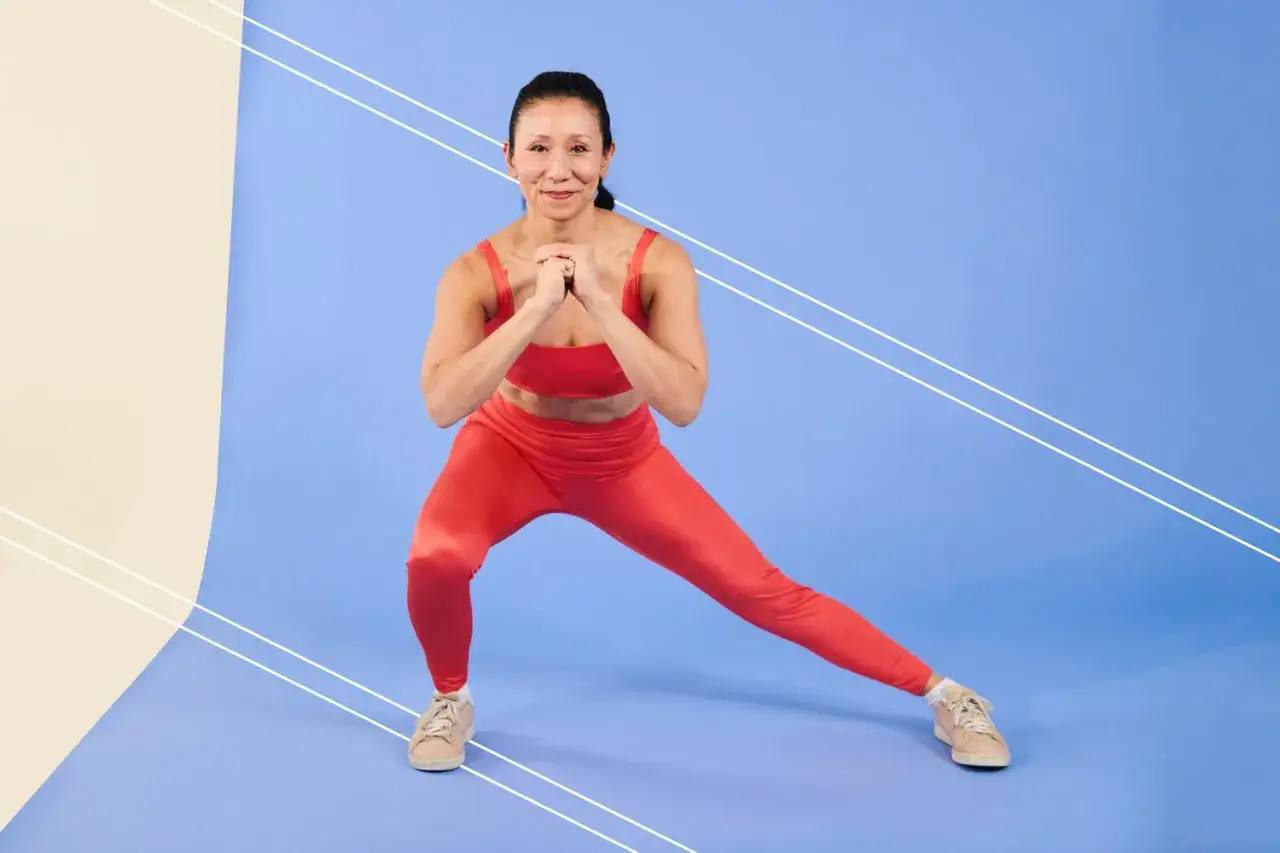 Frau in rotem Sport-Outfit macht seitlichen Ausfallschritt. Trainiert die inneren Oberschenkel, um schwabbelige Oberschenkel innen zu straffen.