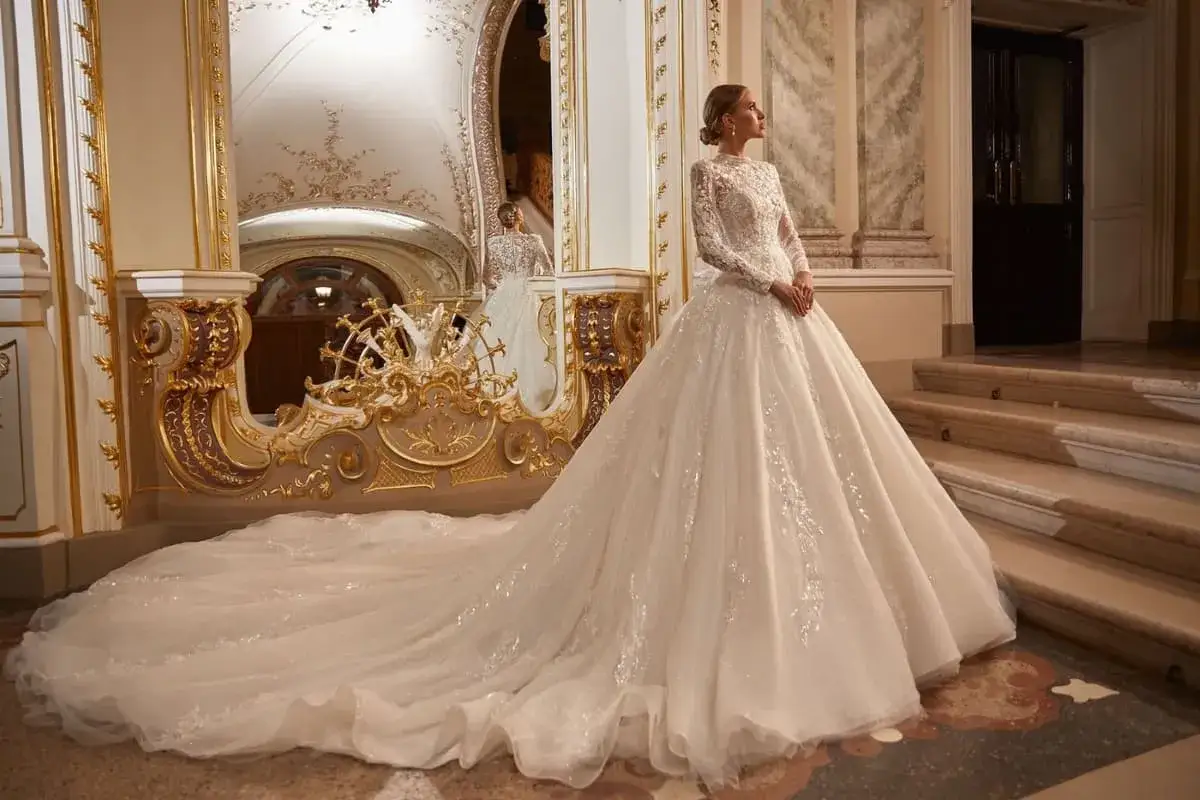 Braut in einem opulenten Kleid, das wie die teuerste Klamotten der Welt aussieht, mit langem Schleier und Spitze, steht in einem prunkvollen Raum.