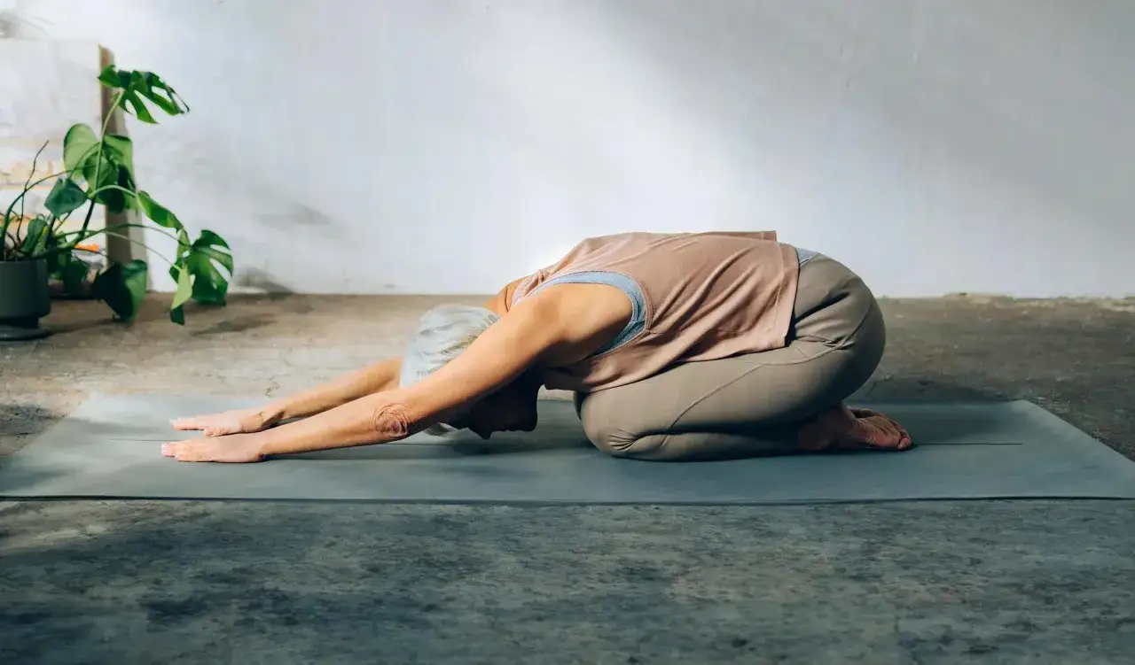 Frau in der Yoga Kindhaltung auf einer Matte, entspannt und mit ausgestreckten Armen.