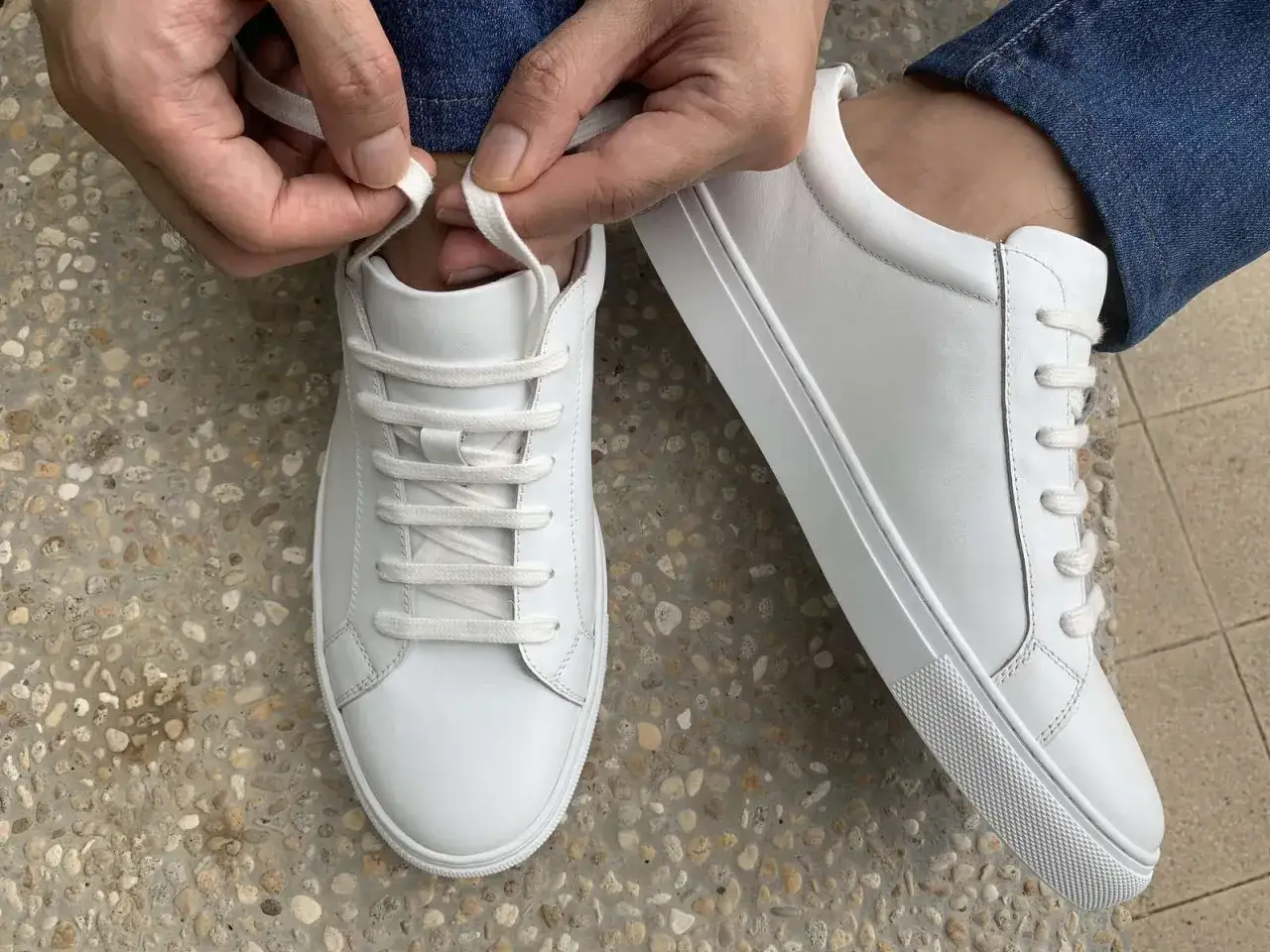 Hände binden die Schnürsenkel der weißen Chucks zu einer Schleife. Die Schnürsenkel verstecken sich geschickt.