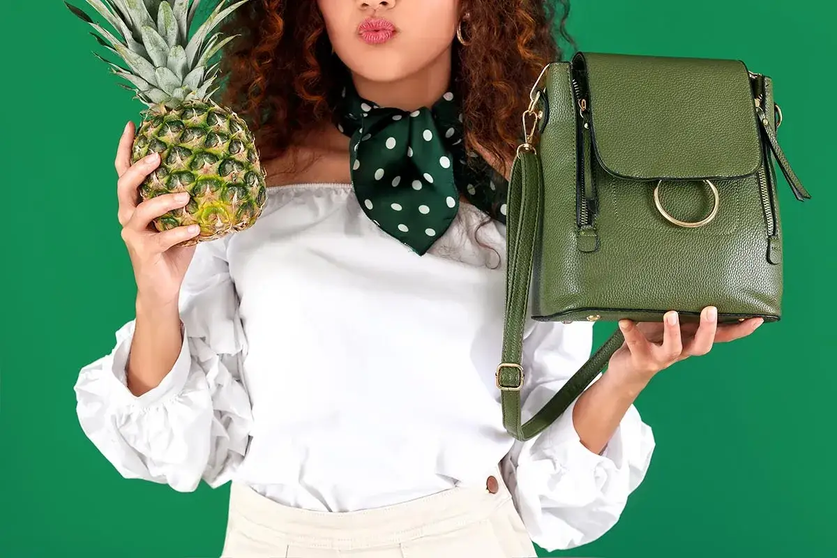 Frau mit Ananas und grüner Tasche, die zeigt, woraus veganes Leder bestehen kann.