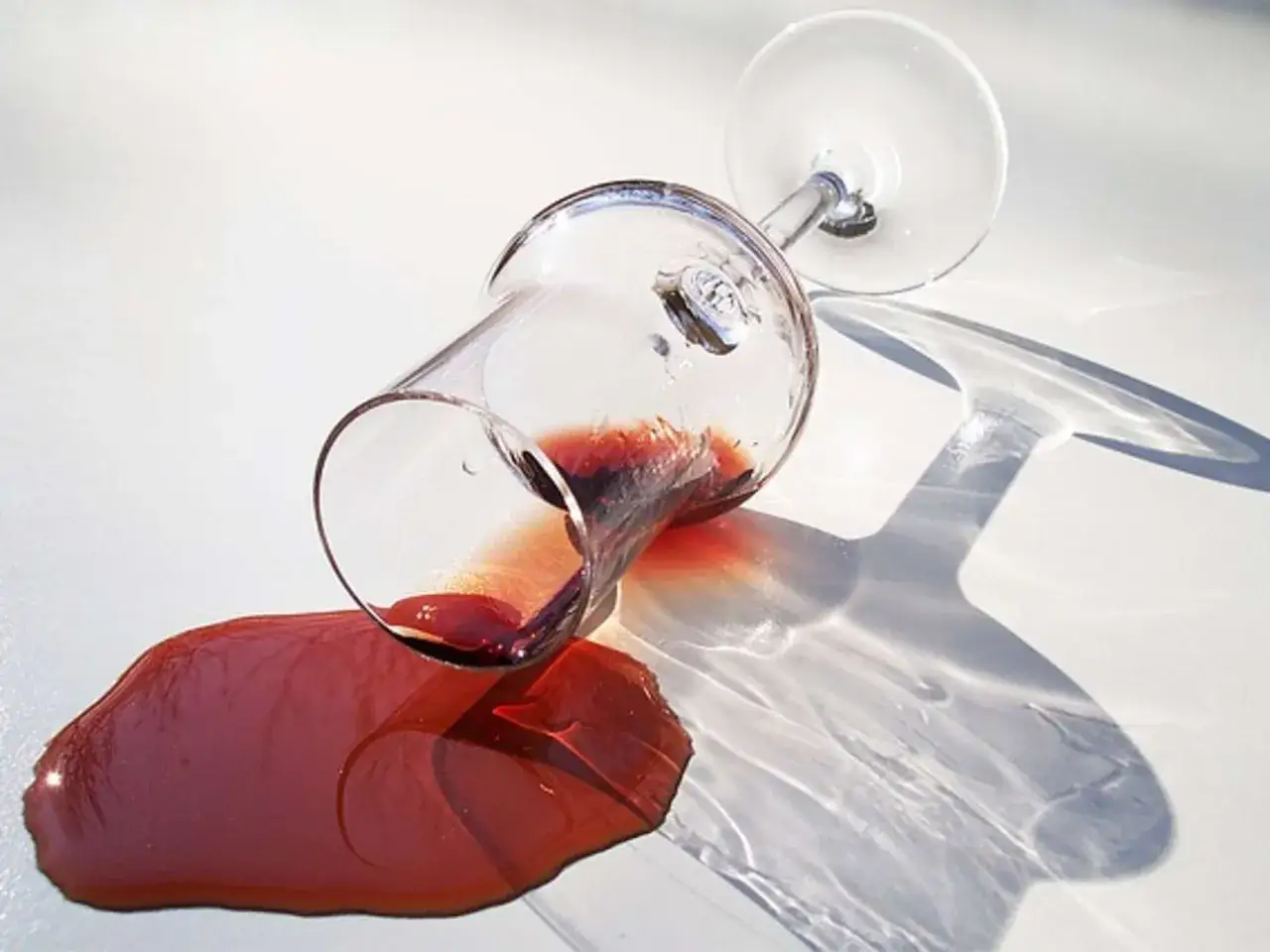 Umgekipptes Weinglas mit Rotwein auf weißer Fläche. Tipps zum wasserflecken entfernen.