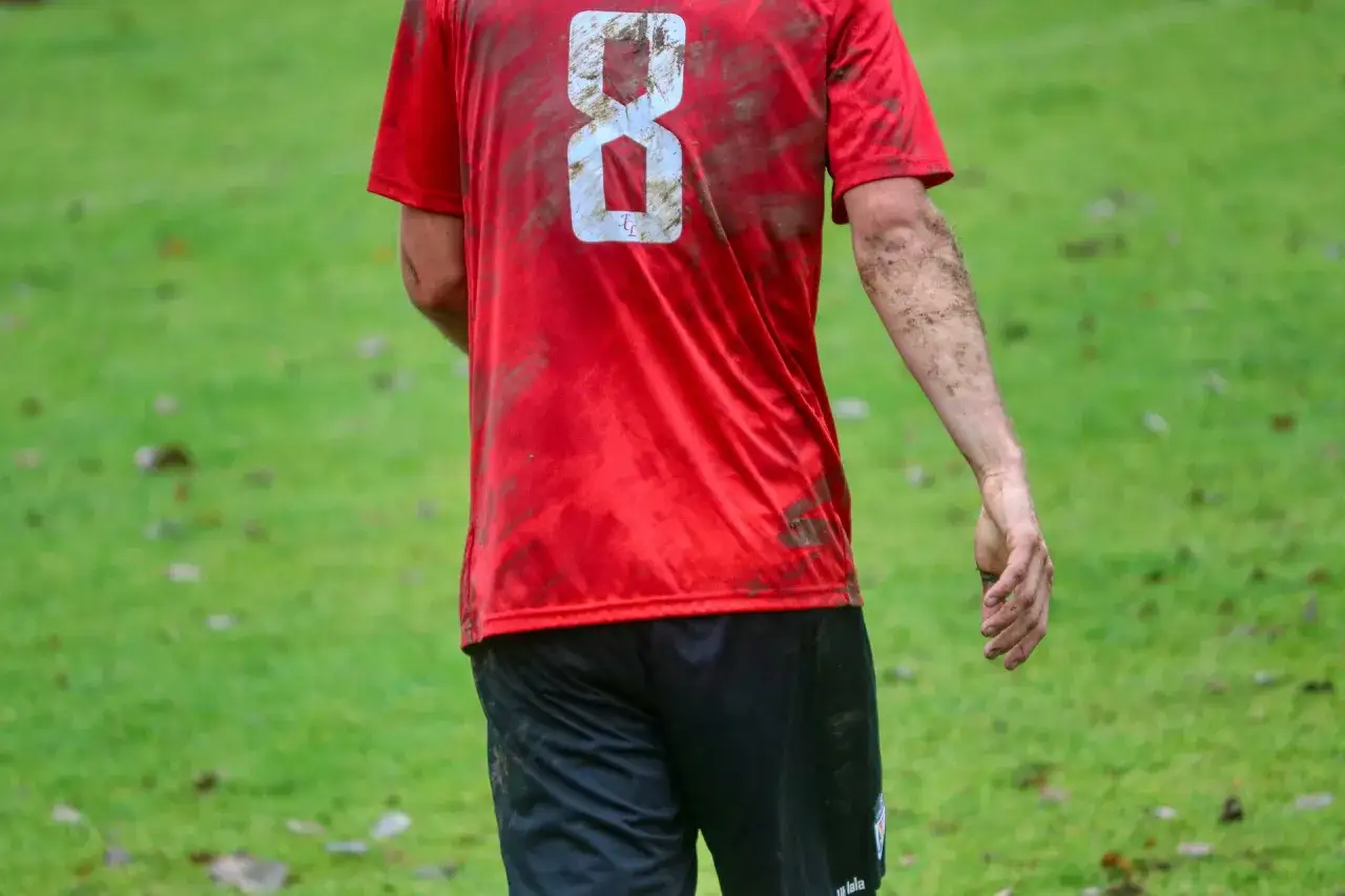 Fußballspieler mit schlammverschmiertem roten Trikot mit der Nummer 8. Nach dem Spiel müssen die trikots gewaschen werden.
