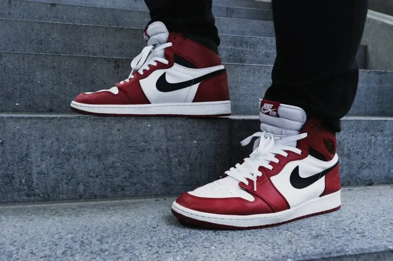 Jordan 1 Mid vs High: Rote und weiße Sneaker mit schwarzem Swoosh auf Steinstufen.