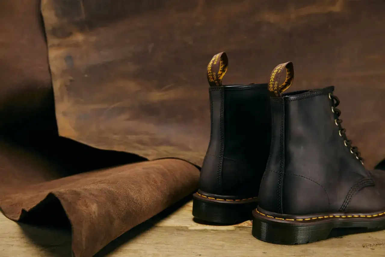 Dr. Martens Stiefel aus dunklem Leder neben einem Stück Rohleder. Die Herkunft des Leders unterstreicht die Qualität.