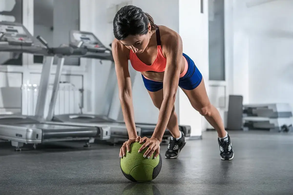 Frau in Sportkleidung trainiert ihre core muskulatur mit einem Medizinball im Fitnessstudio.