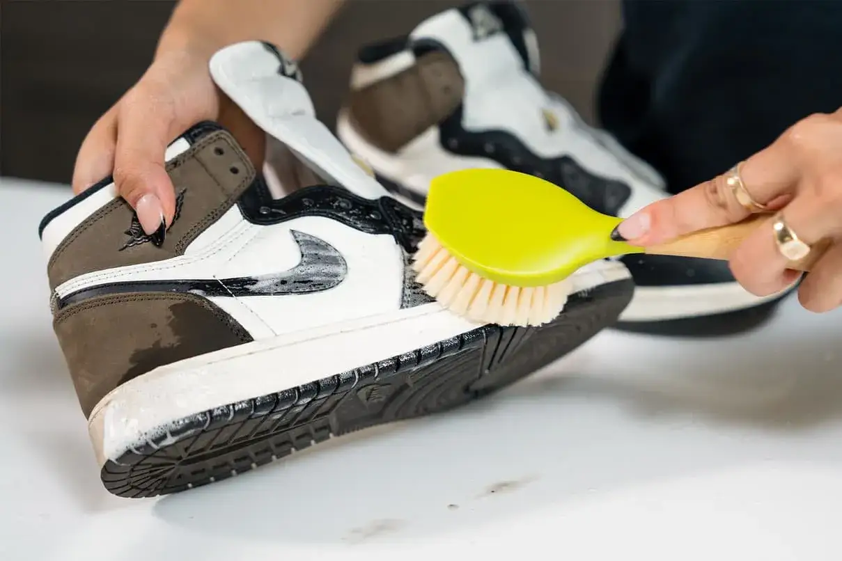 Hände reinigen Turnschuhe mit einer gelben Bürste und Seife.