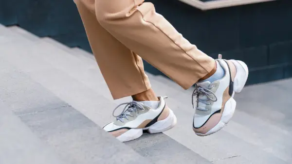 Schritte aufwärts in beigen Hosen und trendigen Sneakern mit sichtbaren Socken. Der socken in sneaker trend ist hier perfekt umgesetzt.