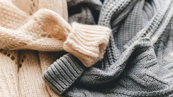 Weiche, gestrickte Pullover in Beige und Grau liegen übereinander. Bald ist Zeit für die **Wolle waschen**, damit sie wieder frisch duften.