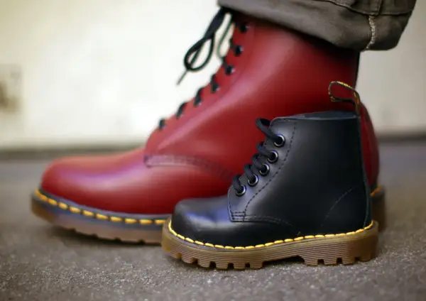 Ein roter und ein schwarzer Dr. Martens Stiefel, die die lange **Dr. Martens Geschichte** von robusten Schuhen für alle Generationen symbolisieren.