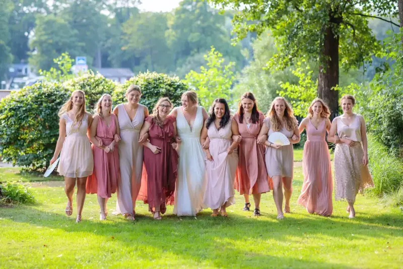 Brautjungfern in zarten Rosatönen, ein perfekter **dresscode hochzeit**, spazieren lachend über eine grüne Wiese.