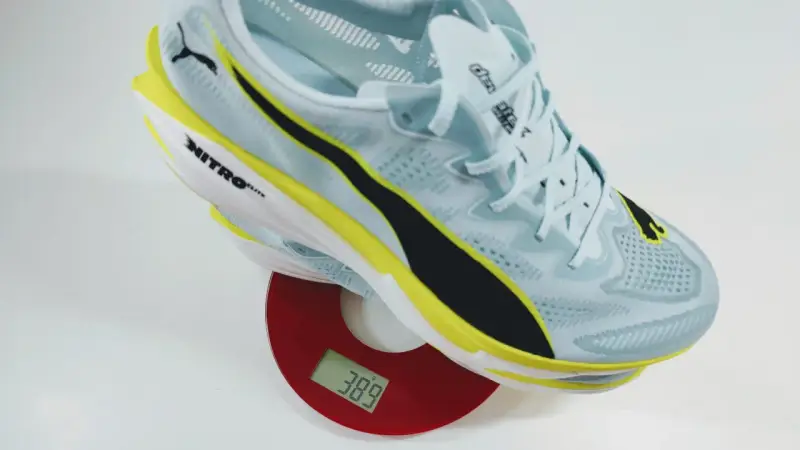 Leichter Laufschuh in Hellblau mit gelben und schwarzen Akzenten auf einer Waage. Das Gewicht der Schuhe beträgt 389 Gramm.