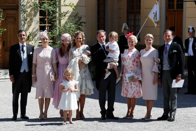 Familie in festlicher Kleidung, die überlegt, was anziehen zur Taufe. Ein Mann trägt ein Baby, Kinder und Frauen in eleganten Kleidern.